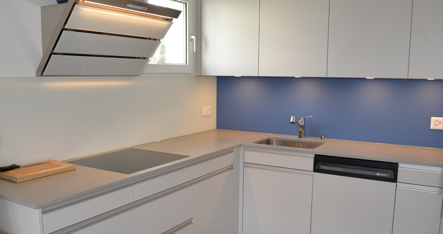 Die relativ enge Küche mit grauen Schränken und einer blauen Rückwand
